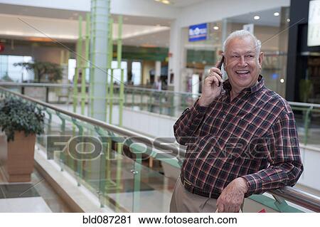 Stock Image - Senior Hispanic man talking on cell phone in mall. Fotosearch