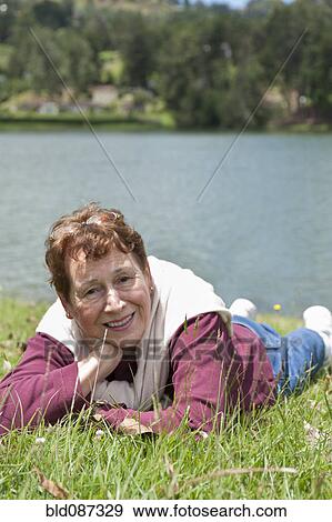Stock Photo - Senior Hispanic woman laying in grass near lake. Fotosearch