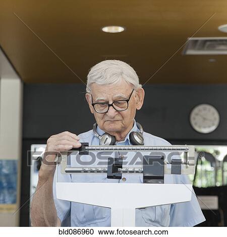 Senior man weighing himself in health club View Large Photo Image Stock Image - Senior man weighing himself in health club. Fotosearch