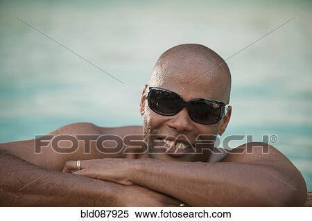 Stock Photography - Smiling African American man leaning on edge of swimming pool. Fotosearch