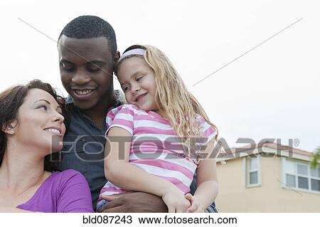 Stock Image - Smiling family hugging outdoors. Fotosearch