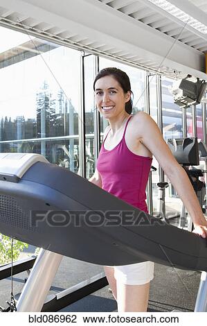 Stock Image - Smiling woman on treadmill in health club. Fotosearch