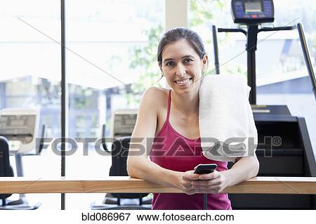 Stock Photo - Woman holding cell phone in health club. Fotosearch