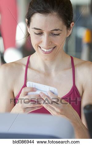 Picture - Woman on treadmill text messaging on cell phone. Fotosearch