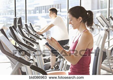 Woman on treadmill text messaging on cell phone View Large Photo Image Stock Image - Woman on treadmill text messaging on cell phone. Fotosearch