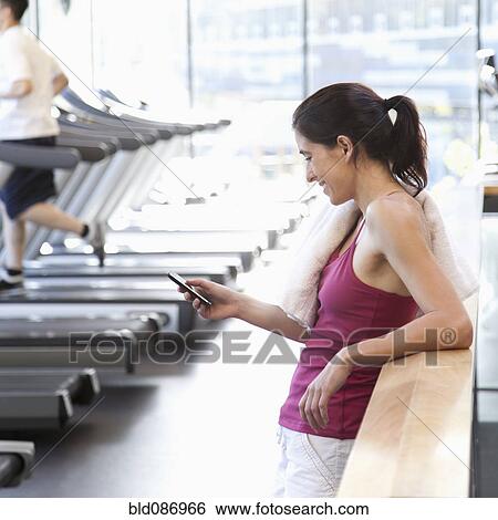 Stock Photograph - Woman text messaging on cell phone in health club. Fotosearch
