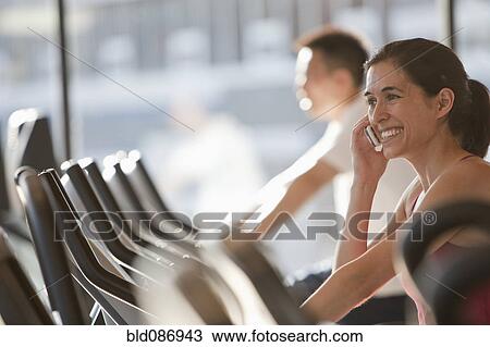 Stock Image - Woman using cell phone on treadmill. Fotosearch