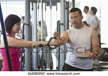 Stock Image - Woman working with personal trainer in health club. Fotosearch