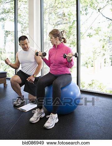 Stock Photo - Woman working with personal trainer in health club. Fotosearch