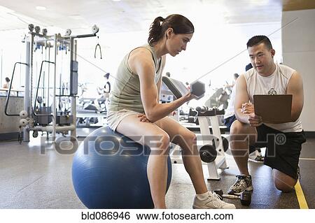 Stock Photograph - Woman working with personal trainer in health club. Fotosearch