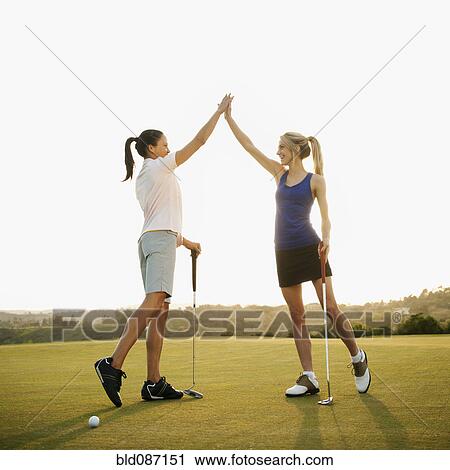 Stock Image - Women golfers high fiving on golf course. Fotosearch