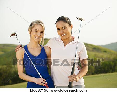 Stock Image - Women with golf clubs hugging on golf course. Fotosearch