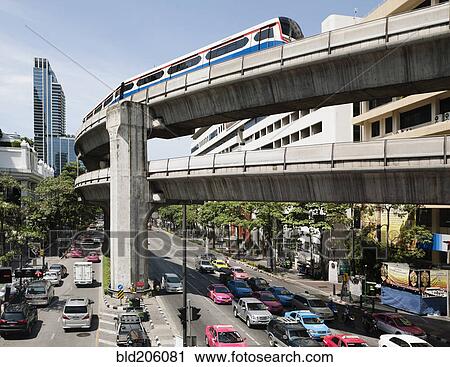Stock Image - A mass transit train on an elevated track passes modern building. Fotosearch