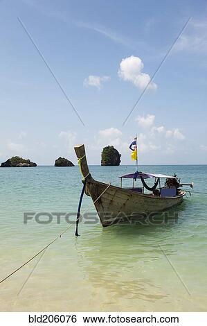 Stock Photograph - A traditional long tail boat moored in shallow water on Tham Phra Nang beach. Fotosearch