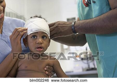 Stock Photograph - African American baby having head bandaged at hospital. Fotosearch