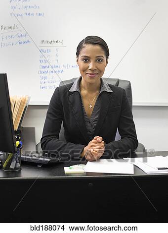 Picture - African American businesswoman sitting at desk in office. Fotosearch