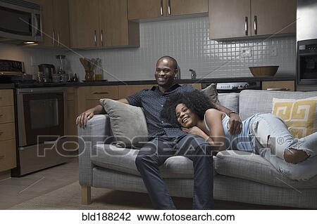 Stock Image - African American couple relaxing on sofa. Fotosearch