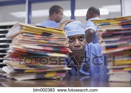 Stock Image - African American doctor looking at stacks of charts. Fotosearch
