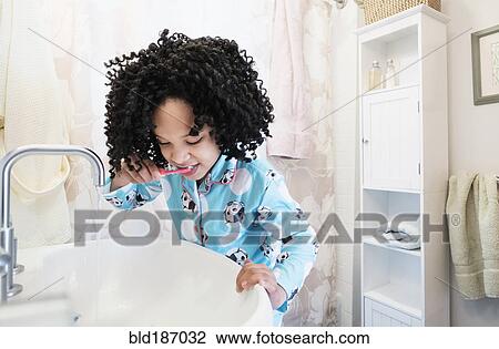 Stock Image - African American girl brushing teeth in bathroom. Fotosearch