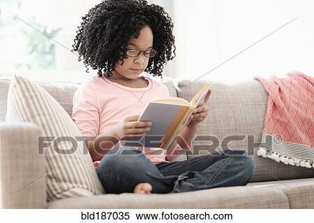 Stock Photography - African American girl reading book on sofa. Fotosearch