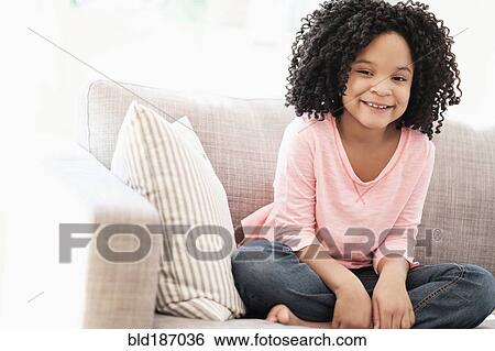 Stock Photograph - African American girl smiling on sofa. Fotosearch