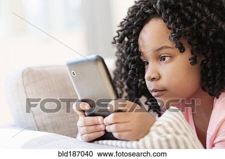 Stock Image - African American girl using cell phone on sofa. Fotosearch
