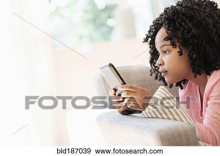 Stock Photo - African American girl using cell phone on sofa. Fotosearch