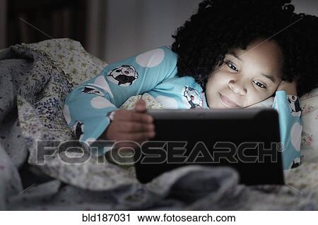 Stock Image - African American girl using digital tablet in bed. Fotosearch