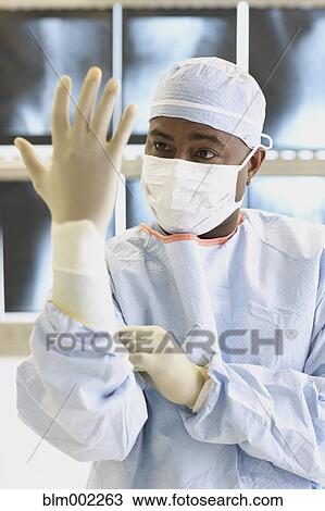 Stock Image - African American male doctor putting on glove. Fotosearch