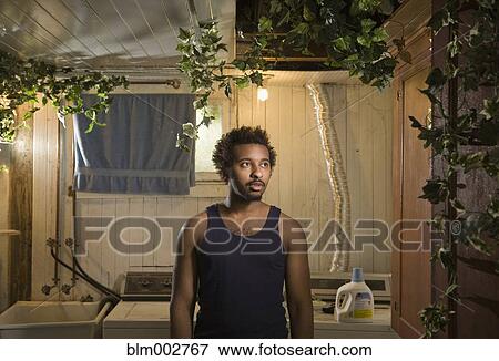 Stock Photo - African American man standing in laundry room overgrown with ivy. Fotosearch