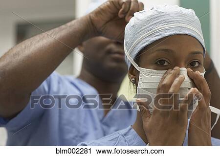 Stock Image - African American medical professional tying coworker's surgical mask. Fotosearch