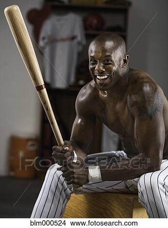 Picture - African baseball player holding bat in locker room. Fotosearch