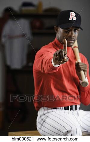 Stock Image - African baseball player making number one gesture in locker room. Fotosearch