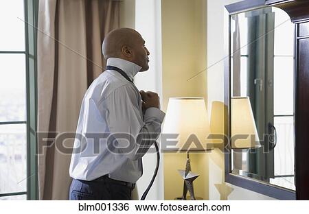 Stock Photograph - African businessman adjusting tie in mirror. Fotosearch