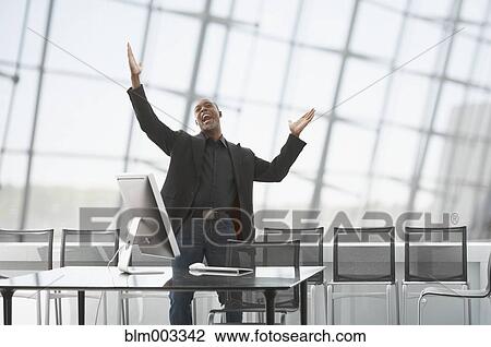 Stock Image - African businessman celebrating in office. Fotosearch