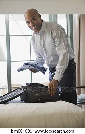 Stock Photography - African businessman in hotel packing suitcase. Fotosearch