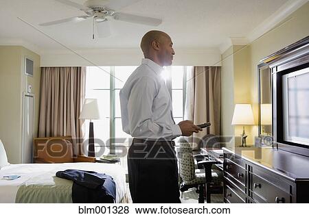 Stock Photo - African businessman in hotel watching television. Fotosearch