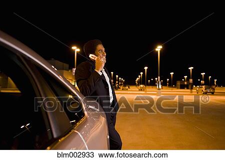 Stock Image - African businessman leaning on car and talking on cell phone. Fotosearch