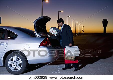 Stock Photo - African businessman loading packages into car in parking lot. Fotosearch