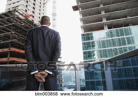 African businessman looking at skyscraper construction from balcony View Large Photo Image Stock Photo - African businessman looking at skyscraper construction from balcony. Fotosearch