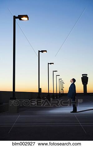 Stock Photo - African businessman looking at street lamp in parking lot. Fotosearch