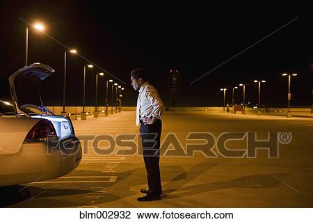 Stock Image - African businessman looking into glowing car trunk in parking lot. Fotosearch