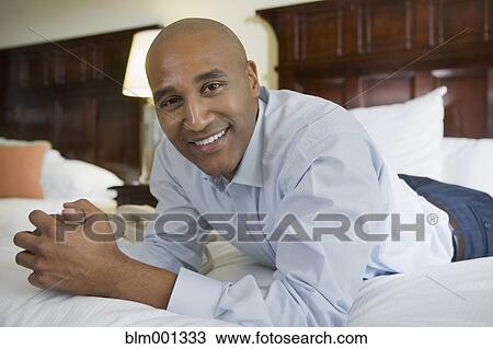 Stock Image - African businessman on hotel bed smiling. Fotosearch