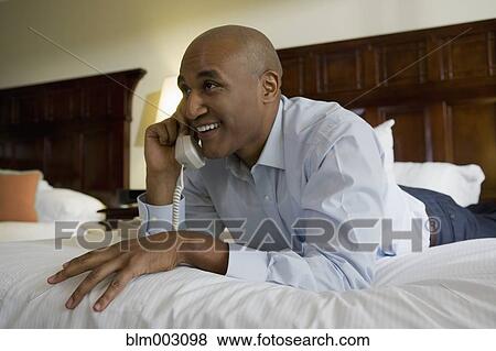 Stock Photo - African businessman on hotel bed using telephone. Fotosearch