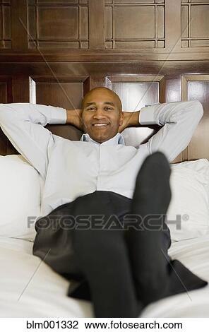 Stock Image - African businessman relaxing on bed. Fotosearch