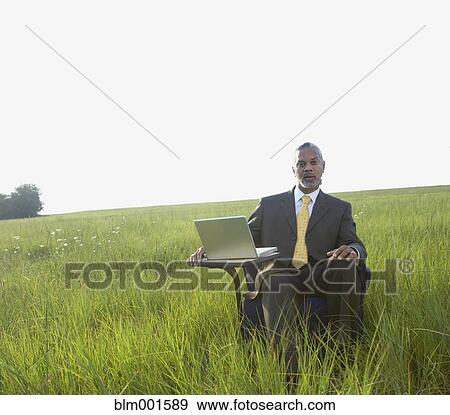Stock Photo - African businessman sitting with laptop in field. Fotosearch