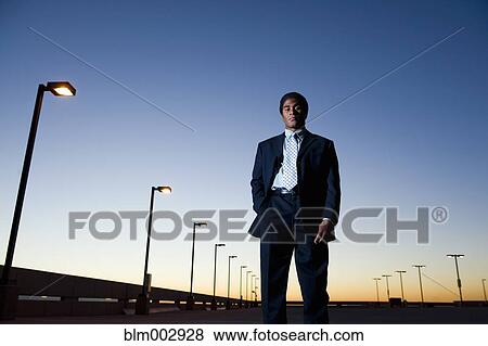 Stock Photo - African businessman standing in parking lot at night. Fotosearch