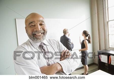 African businessman with arms crossed and co-workers in background View Large Photo Image Stock Photography - African businessman with arms crossed and co-workers in background. Fotosearch