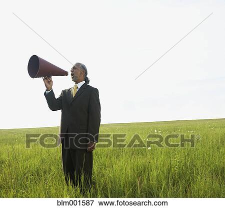 Stock Photo - African businessman yelling through megaphone in field. Fotosearch