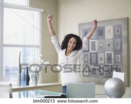 Stock Image - African businesswoman cheering in office. Fotosearch